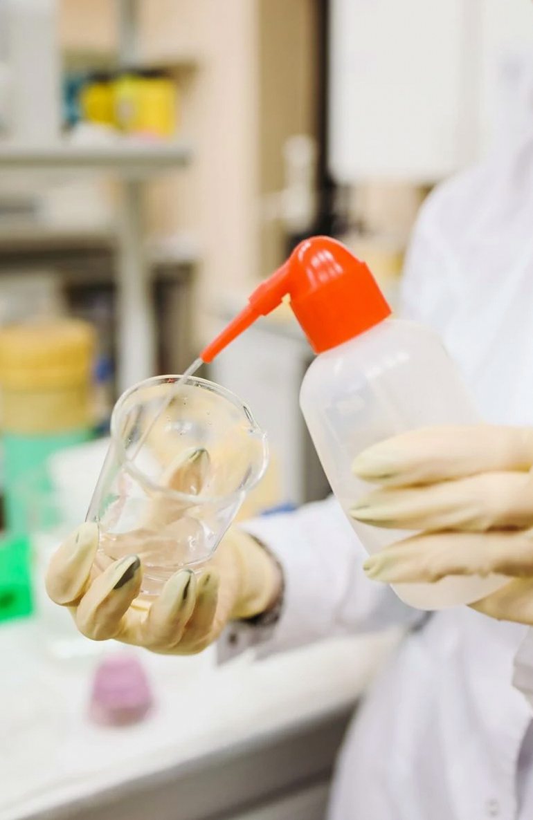 Scientist carefully pouring liquid into a beaker in a laboratory setting, wearing protective gloves.